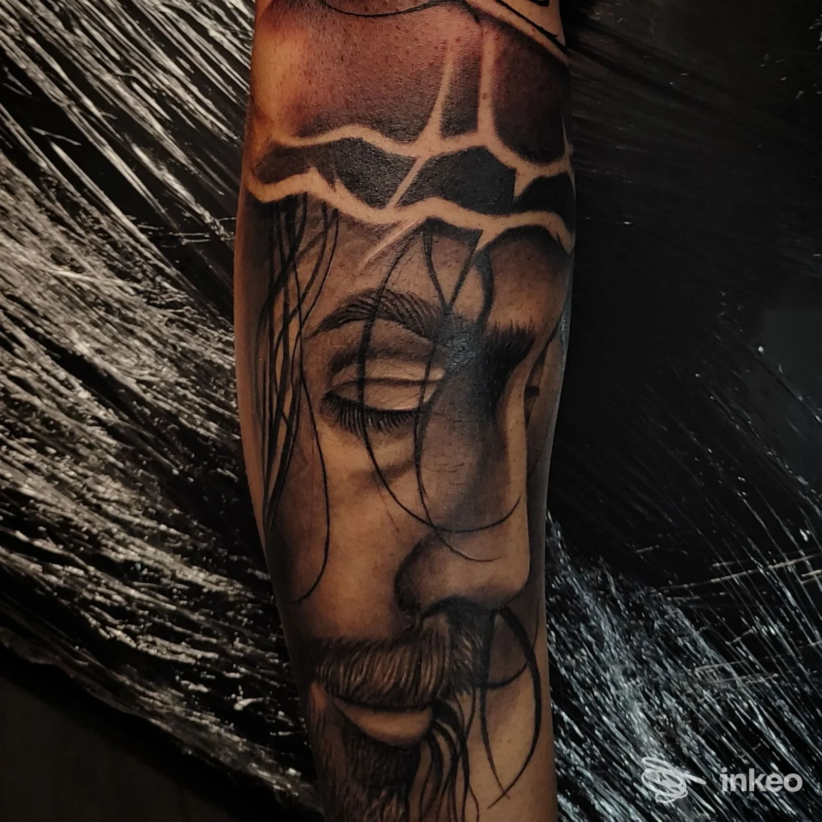 Fotografia di un braccio con un tatuaggio realistico di un volto e linee astratte sullo sfondo, realizzato nello studio Old Skull Tattoo Lab a Fisciano.