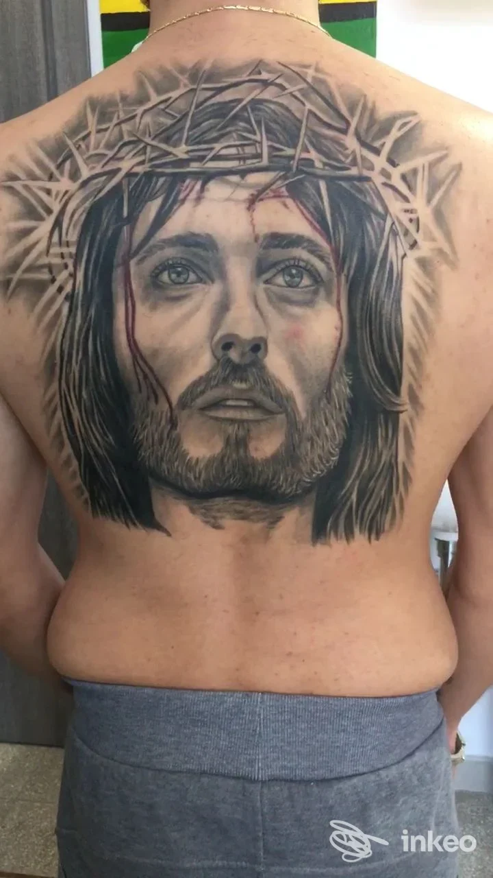Tattoo realistico in bianco e nero sulla schiena raffigurante Gesù Cristo con corona di spine, visibile la pelle e i contorni dell’opera.