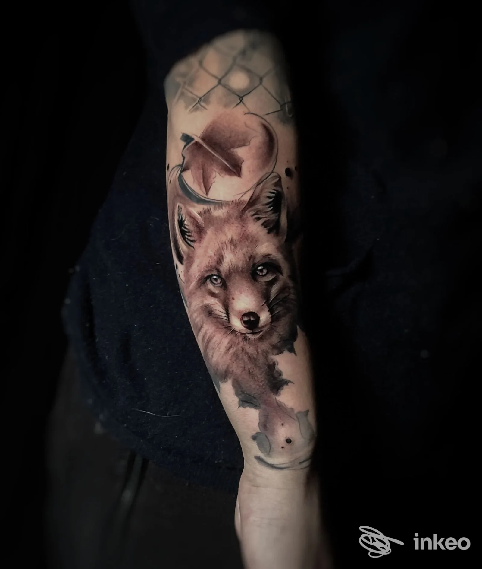 Avambraccio con tatuaggio realistico di una volpe, con luna crescente sullo sfondo; tonalità scure e sfumature nere e grigie, sfondo scuro.