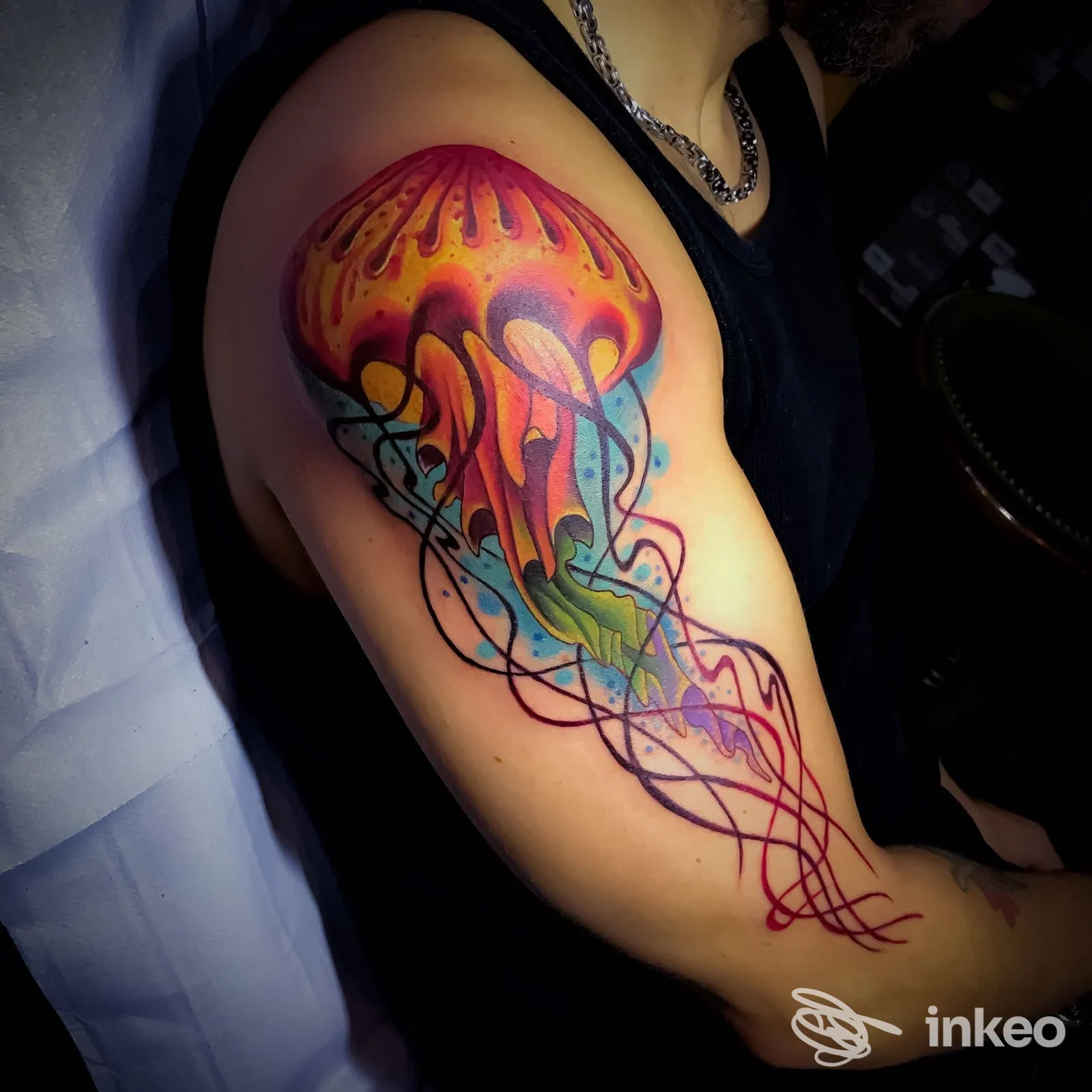 Tatuaggio a colori di una medusa stilizzata sul braccio di una persona, realizzato sulla pelle in uno studio, senza viso visibile.