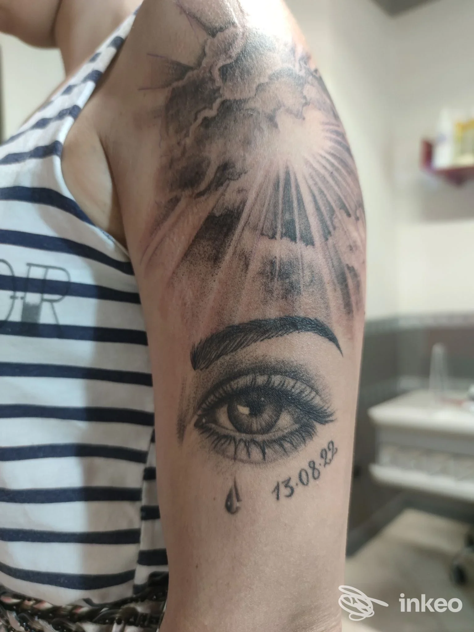 Parte superiore del braccio con un tatuaggio realistico che raffigura un occhio, una lacrima e la data, realizzato da Nifra Tattoo a Camposano.