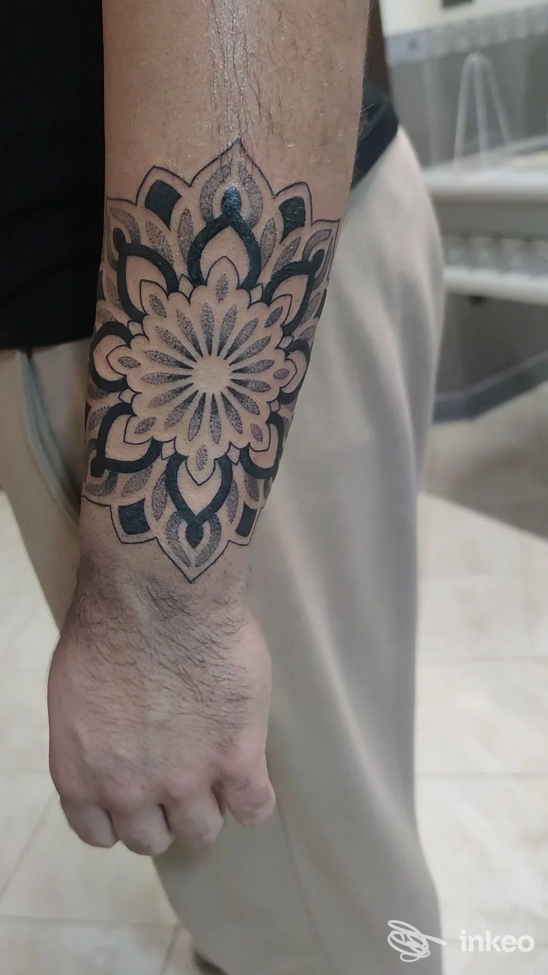 Tattoo geometrico a mandala sull’avambraccio sinistro, con linee nere e sfumature, visibile su pelle chiara, braccio al lato.
