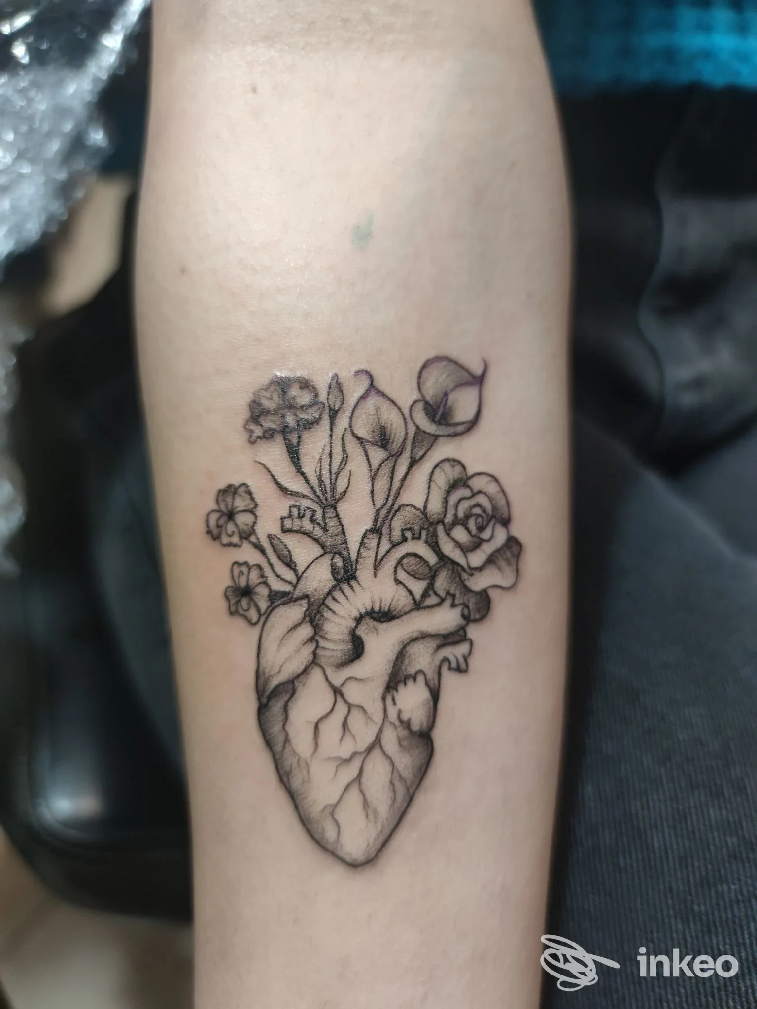 Tatuaggio realistico a forma di cuore anatomico, con fiori e boccioli, inciso sull'avambraccio destro. Studio Nifra Tattoo, Camposano.