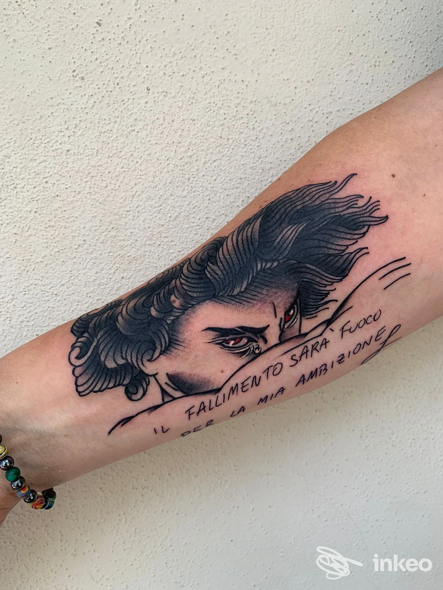 Braccio con tatuaggio visibile: ritaglio di una figura stilizzata con linee nette e testo italiano sul braccio, senza elementi di interfaccia sociale; studio South Ink Tattoo Shop a Pozzuoli.