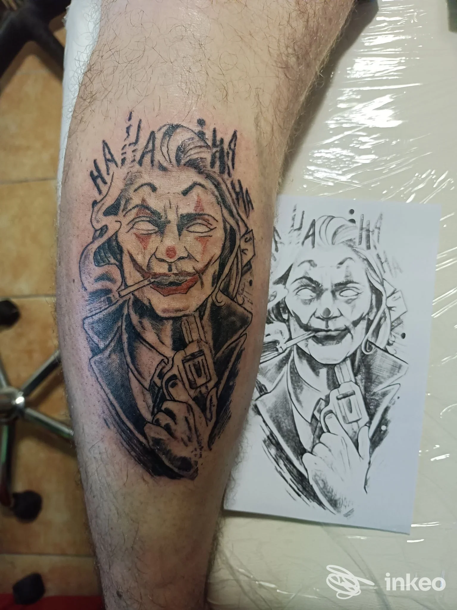 Tattoo su pelle raffigurante una figura clown con espressione intensa, realizzata sul polpaccio; accanto una stampa stencil bianco e nero.