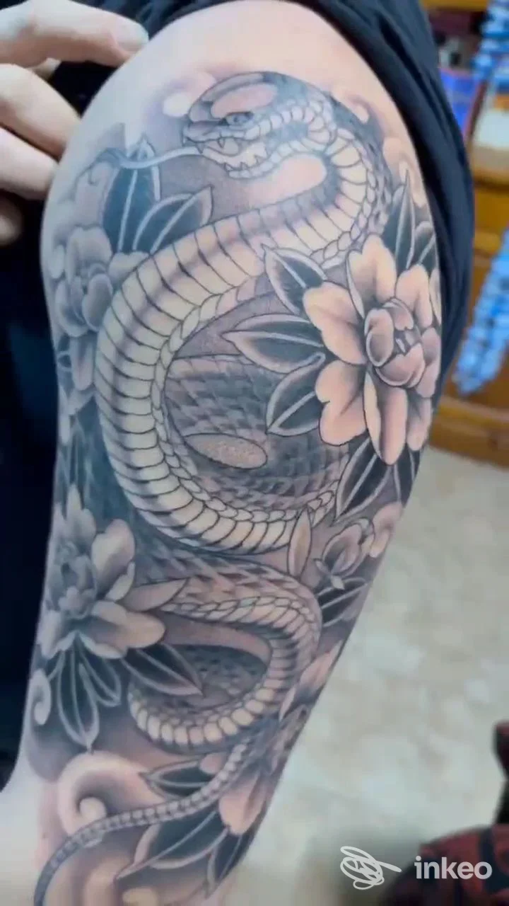 Tatuaggio realistico in nero grigio di una serpente avvolta tra fiori, visibile sul braccio; nessun volto o testo promozionale presente.