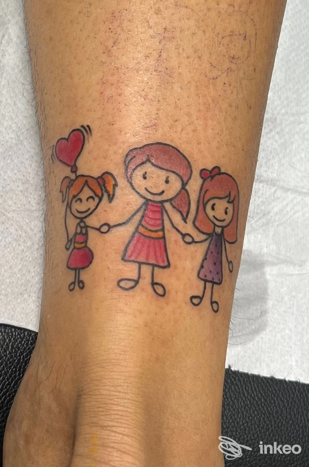 Tattoo su avambraccio raffigurante tre bambine stilizzate che tengono le mani, colori vivaci (rosso, rosa, arancio) con contorni neri. Studio Vitale Tattoo, Napoli.