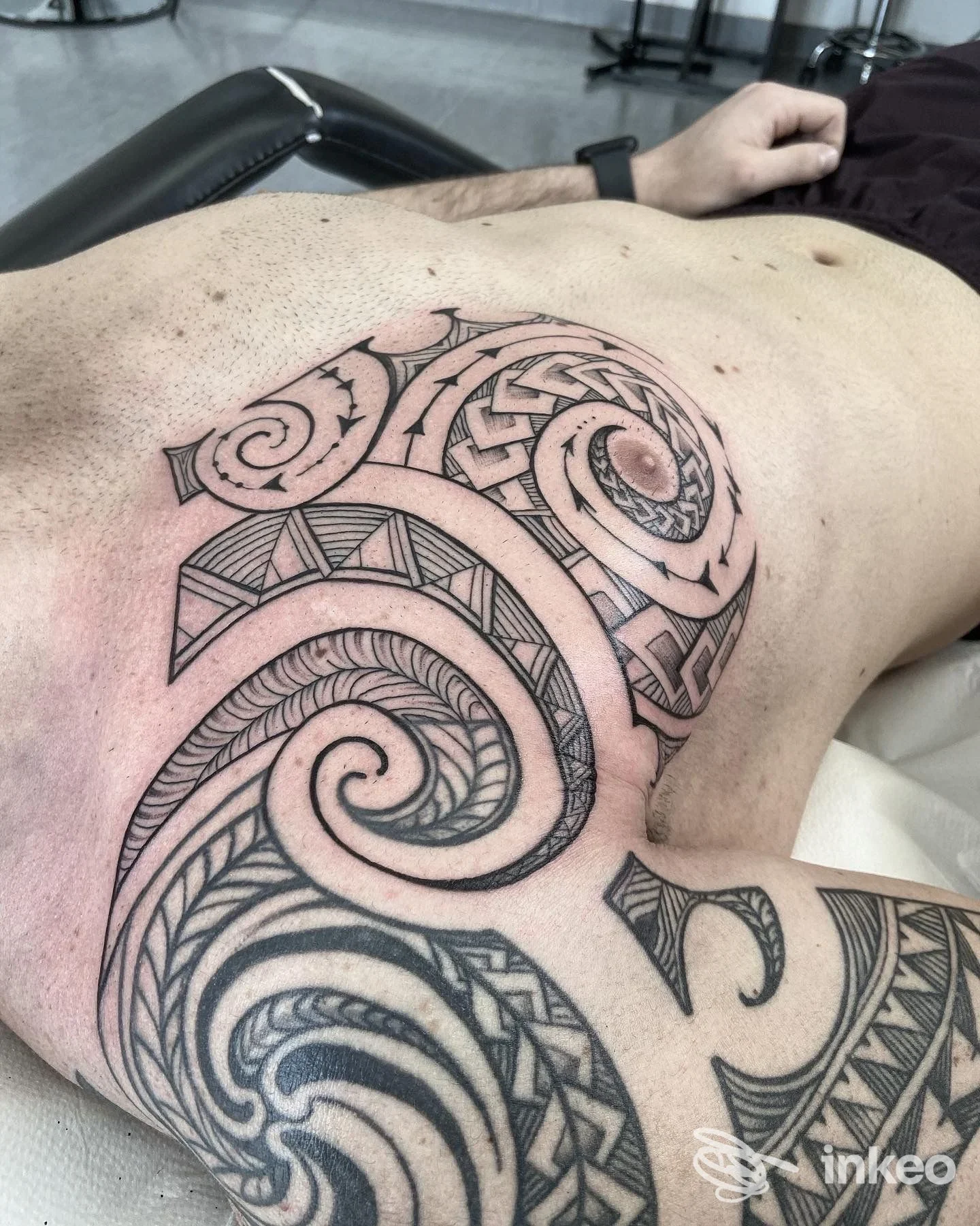 Tattoo geometrico-tribale su torace, inchiostrato in bianco e nero con linee e motivi intricati, senza viso visibile