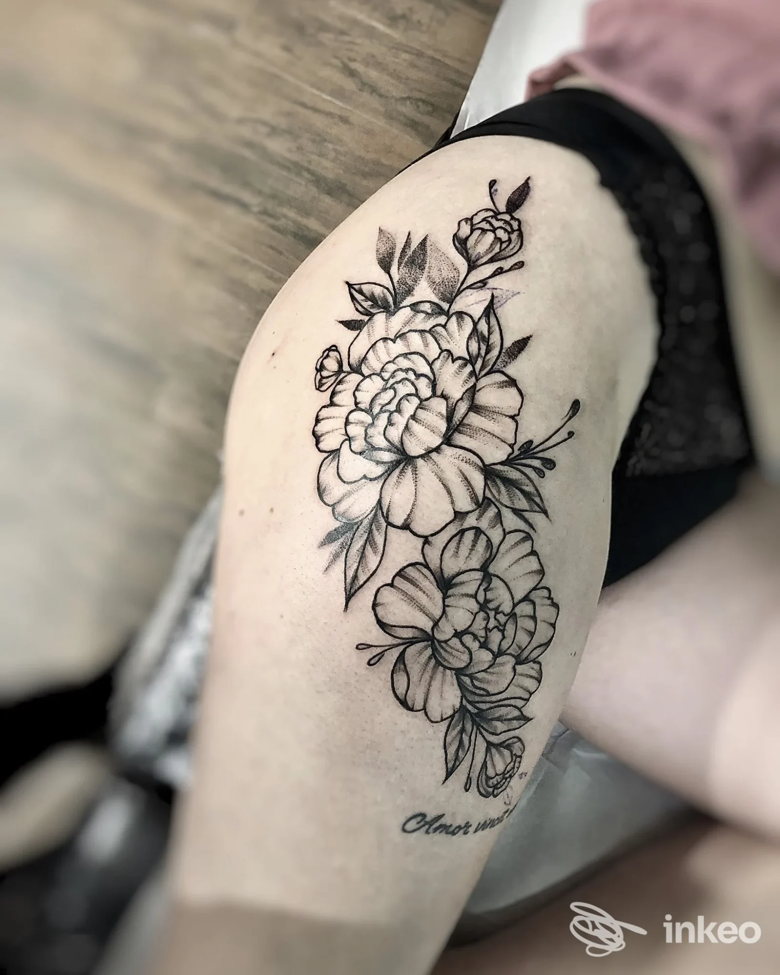 Tattoo floreale in stile linework su braccio di una persona, disegno nero su pelle, senza volto visibile, sfondo sfumato.