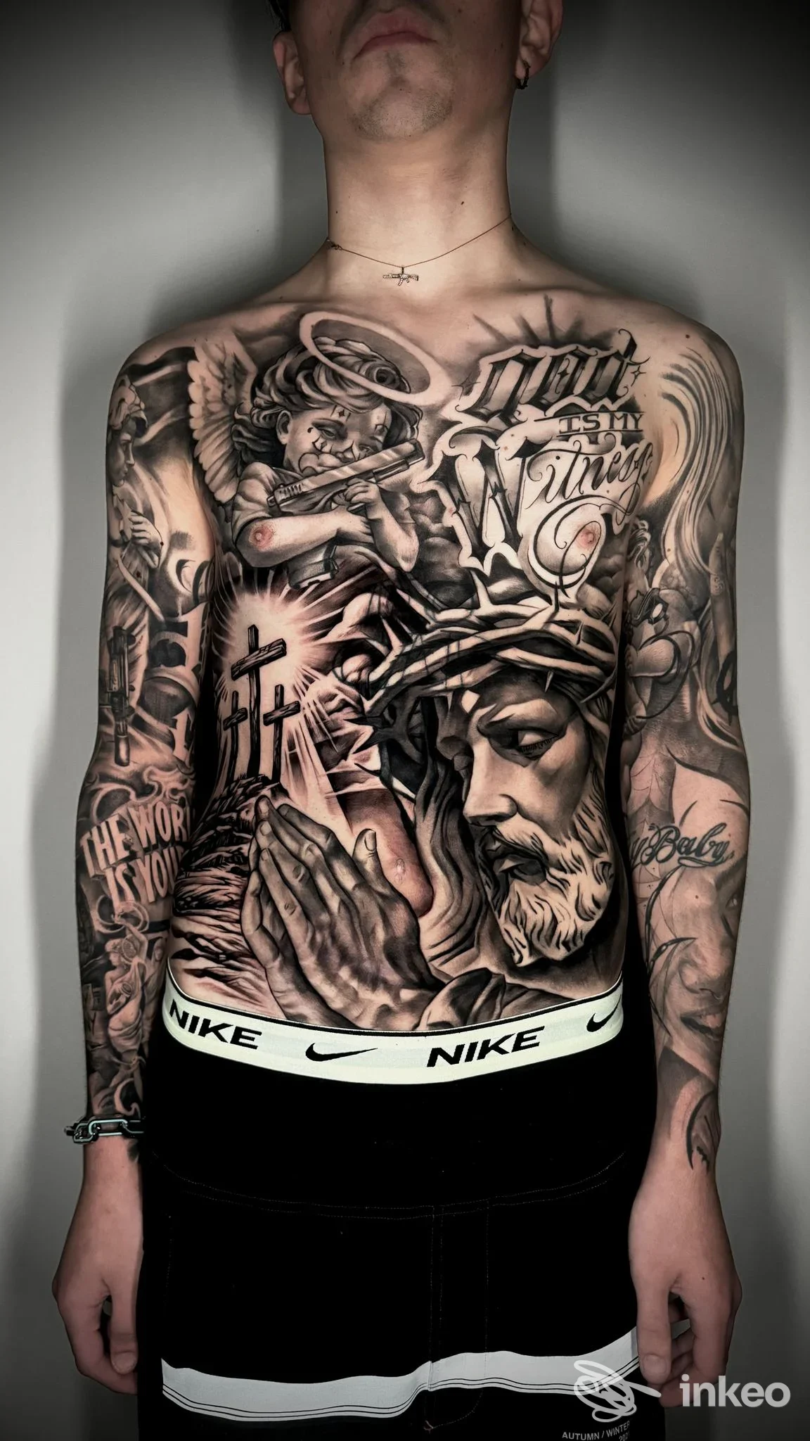 Torace e braccia completamente tatuati in stile noir, con figure e testi, viso parzialmente visibile dall'angolo inferiore, in studio inkllusion a Casoria.