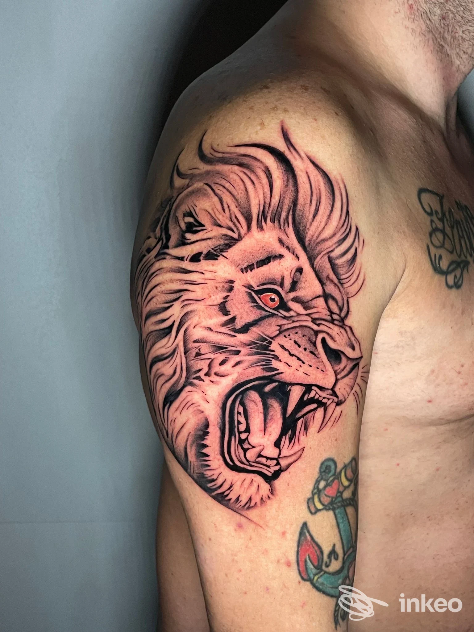 Tattoo a braccio raffigurante una testa di leone, stile grafico realistico con linee nere e sfumature rosse, visibile la pelle e parte del torace del soggetto.