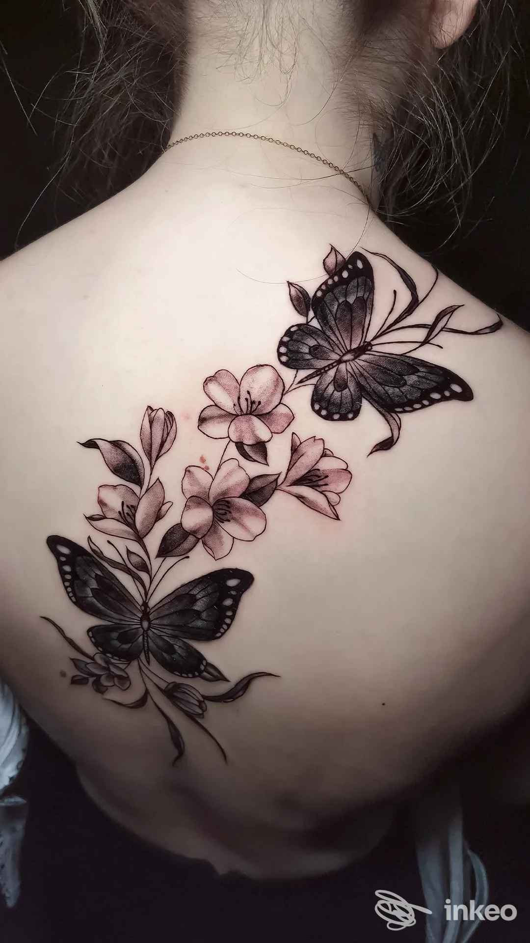 Tattoo visibile sulla spalla/alta schiena: una catena di farfalle nere con fiori rosa delicati, eseguita sulla pelle della persona.