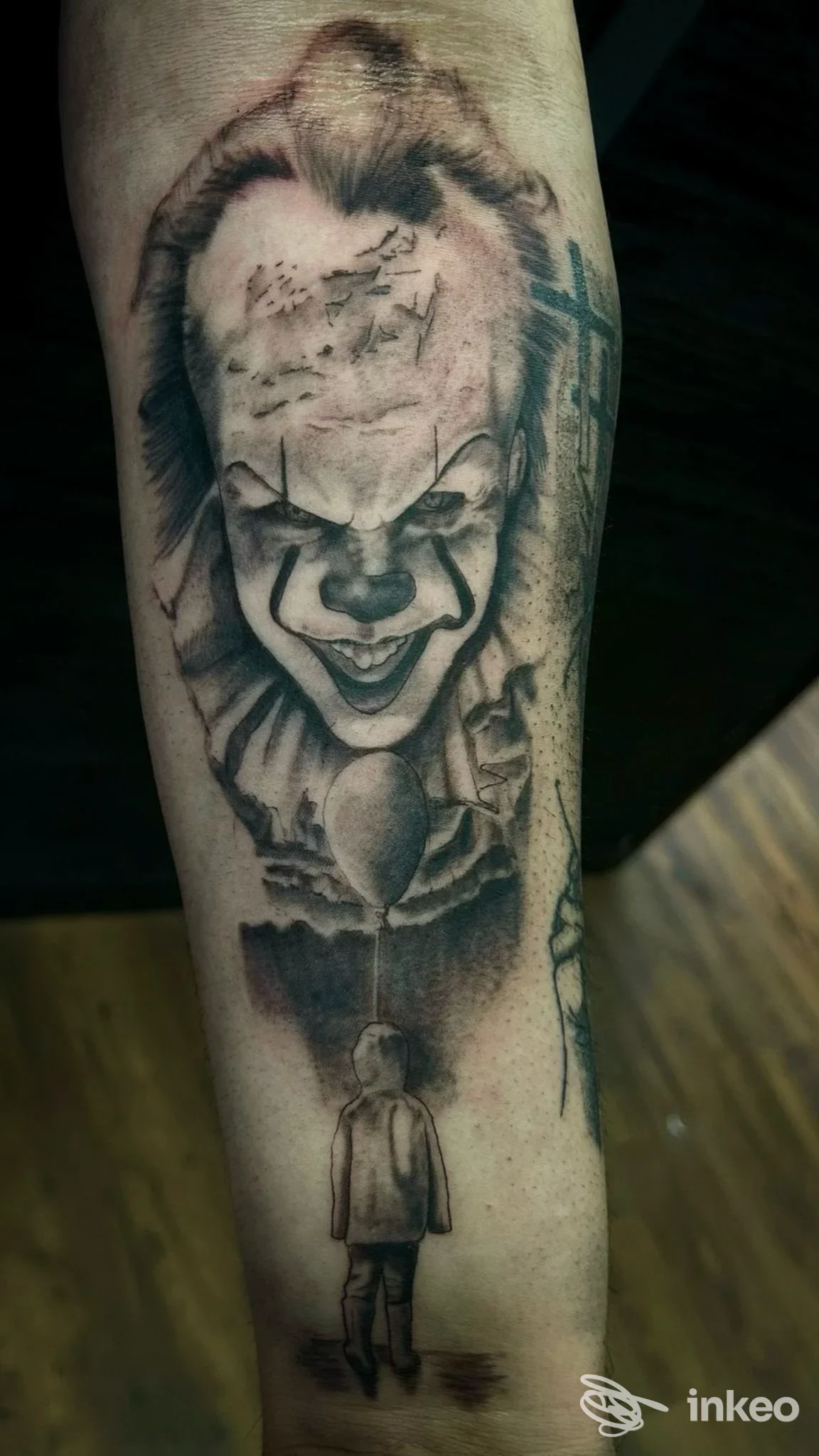 Tattoo realistico sul braccio raffigurante Pennywise, con figura di bambino in primo piano, realizzato dal Black Side Tattoo Studio a Cesa.