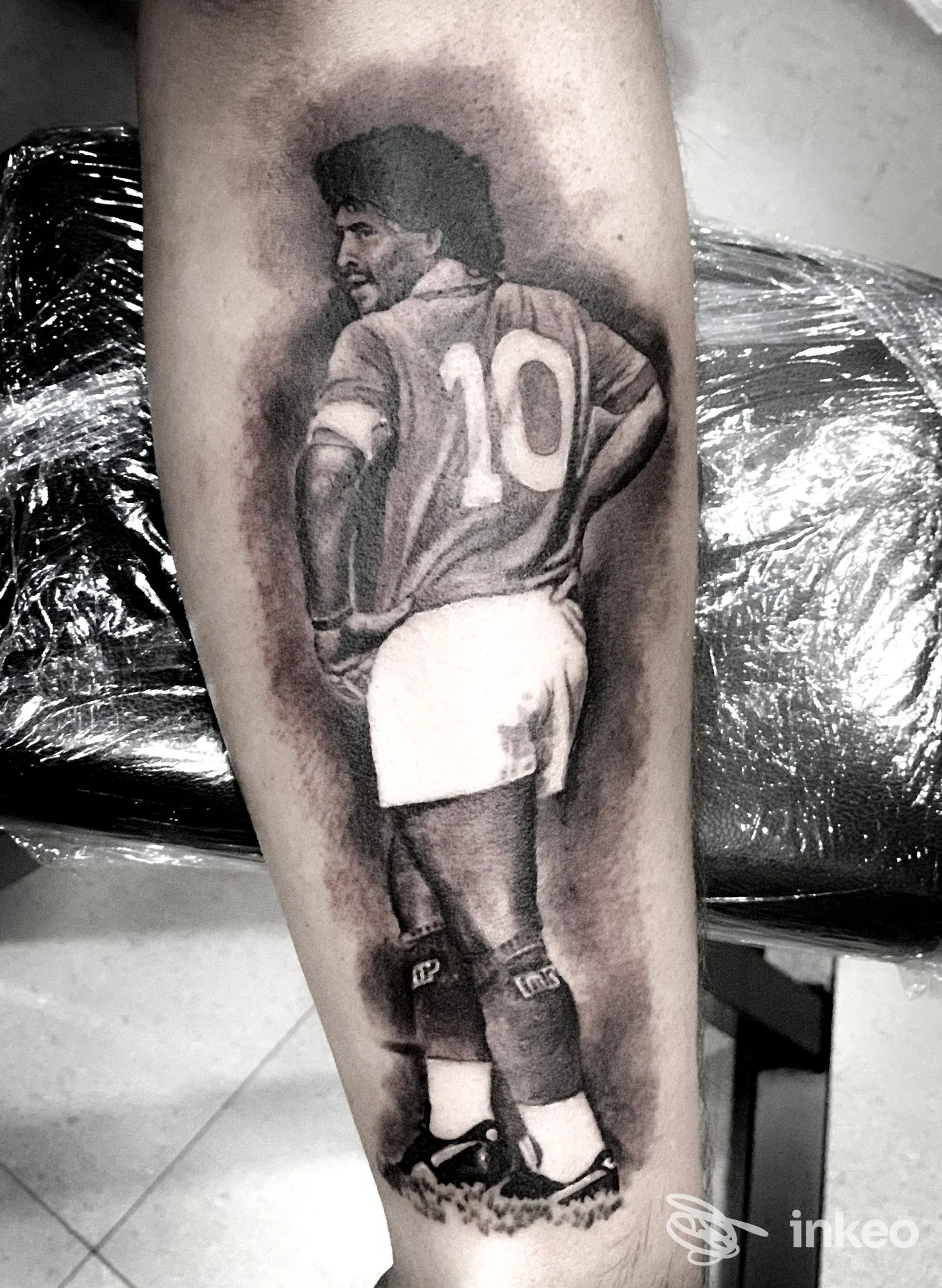 Tattoo realistico in bianco e nero di un giocatore di calcio con la maglia numero 10 sulla gamba, ritratto da dietro.
