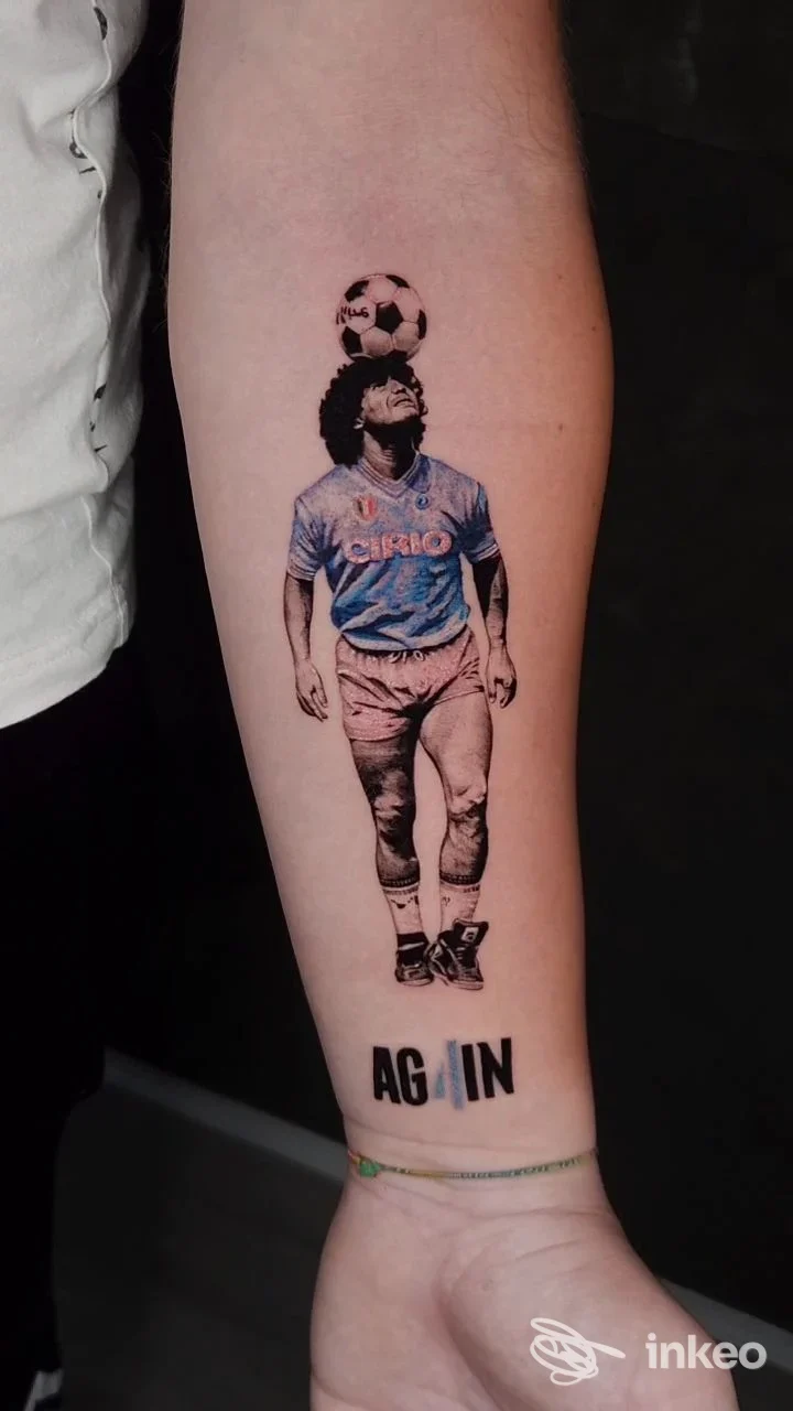 Tatuaggio visibile nella parte inferiore della gamba: un calciatore con la maglia azzurra tiene un pallone sulla testa, silhouette molto nitida su pelle chiara.