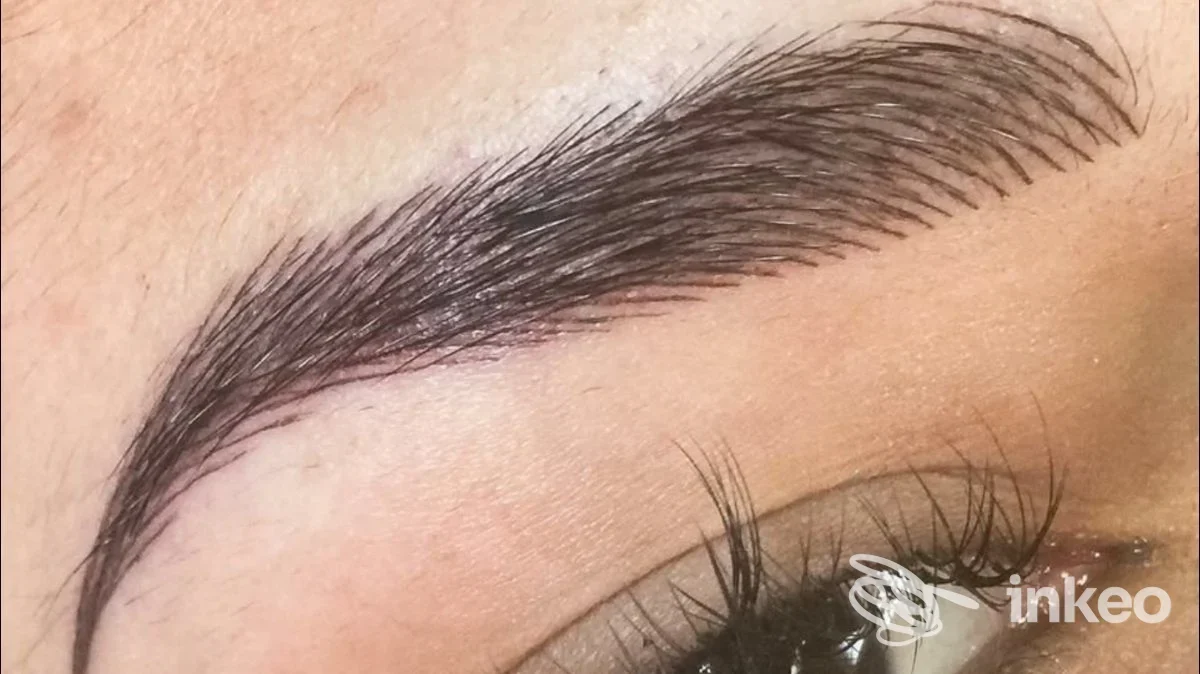 Sopracciglio dermopigmentato visibile su pelle, primo piano vicino all'occhio con tratto illeso e texture della pelle.