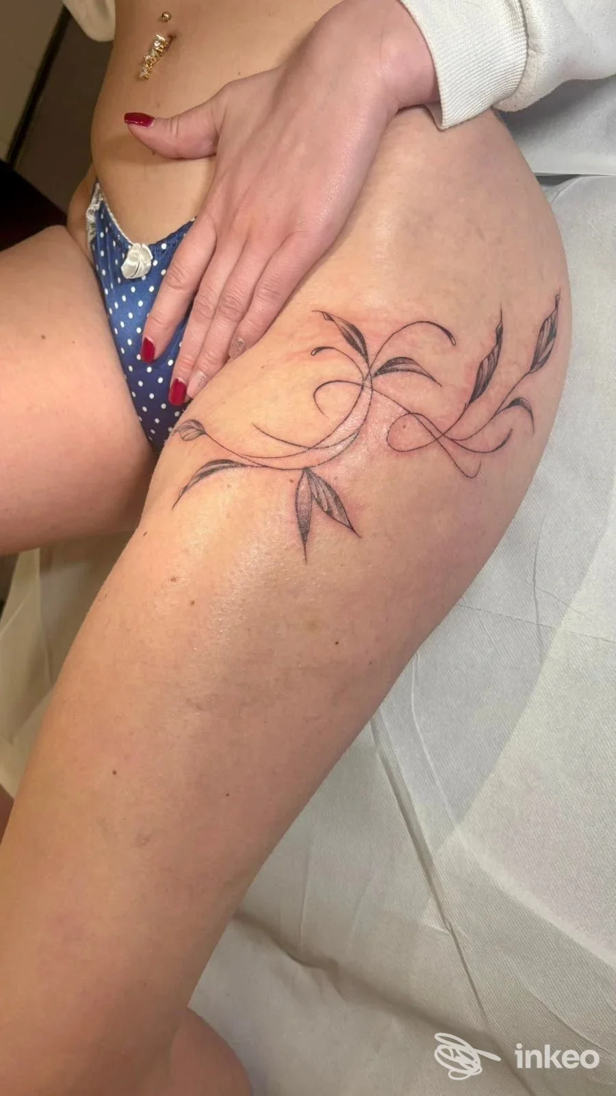 Tattoo floreale in stile disegno a linee sul fianco della coscia sinistra, eseguito su pelle, con tonalità scure.