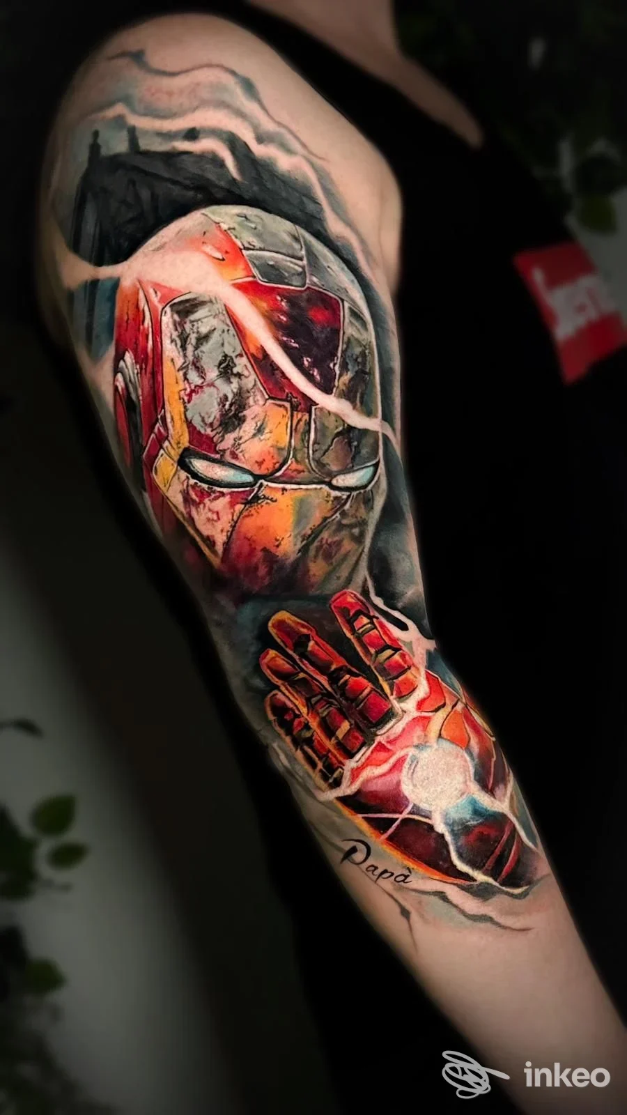 Braccio sinistro con tatuaggio colorato e dettagli realistici, senza volto visibile, in un contesto studio.