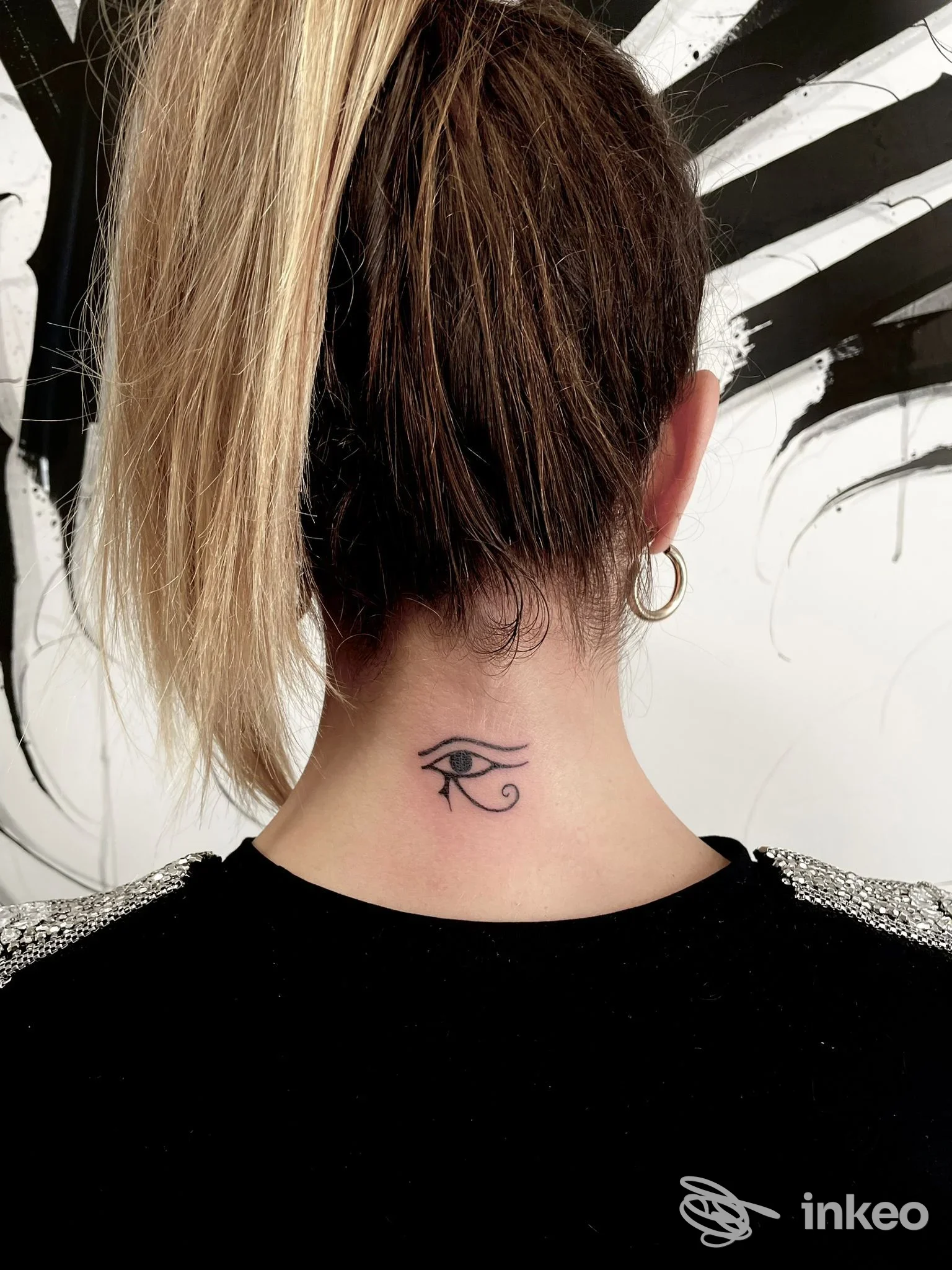 Tattoo sull’avambraccio della nuca raffigurante l’occhio di Horus, visibile sulla nuca di una modella, con capelli colorati, orecchino a cerchio.