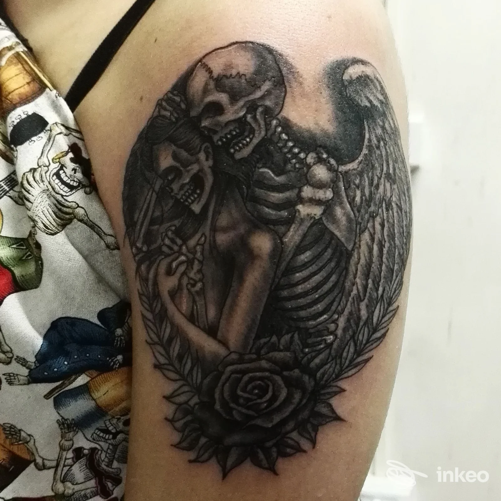 Tattoo sul braccio raffigurante due scheletri abbracciati con un'aurora di ali e una rosa centrale, lavorata in stile black and gray, eseguita in uno studio di Aversa, Anima sottopelle Tattoo Store.