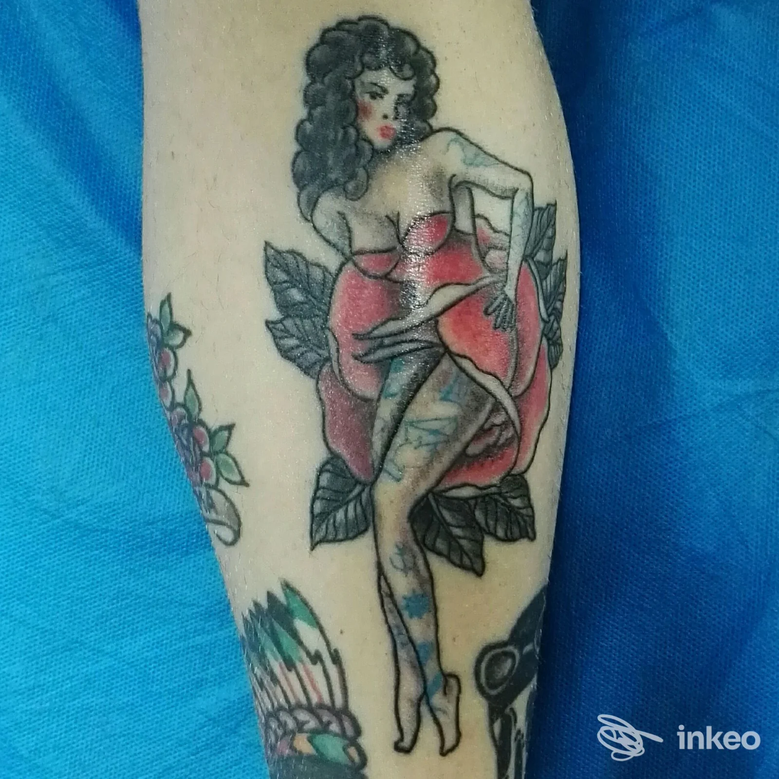 Tattoo visibile su una gamba raffigurante una donna con capelli ricci, vestito rosso, sfondo floreale; stile old school, colori vividi.