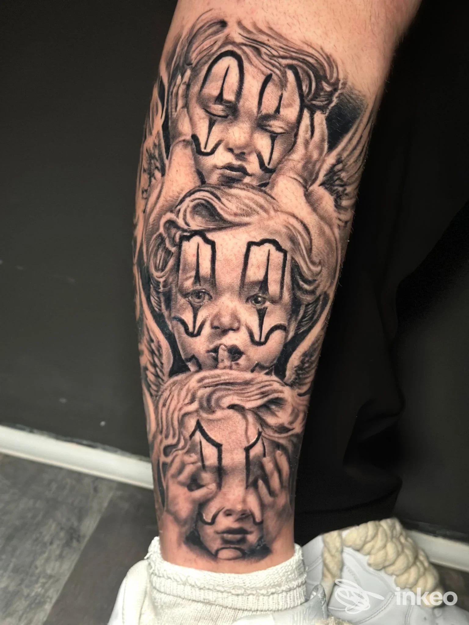 Tatuaggio su gamba raffigurante tre volti stilizzati con trucco da clown, in bianco e nero, realizzato direttamente sulla pelle.