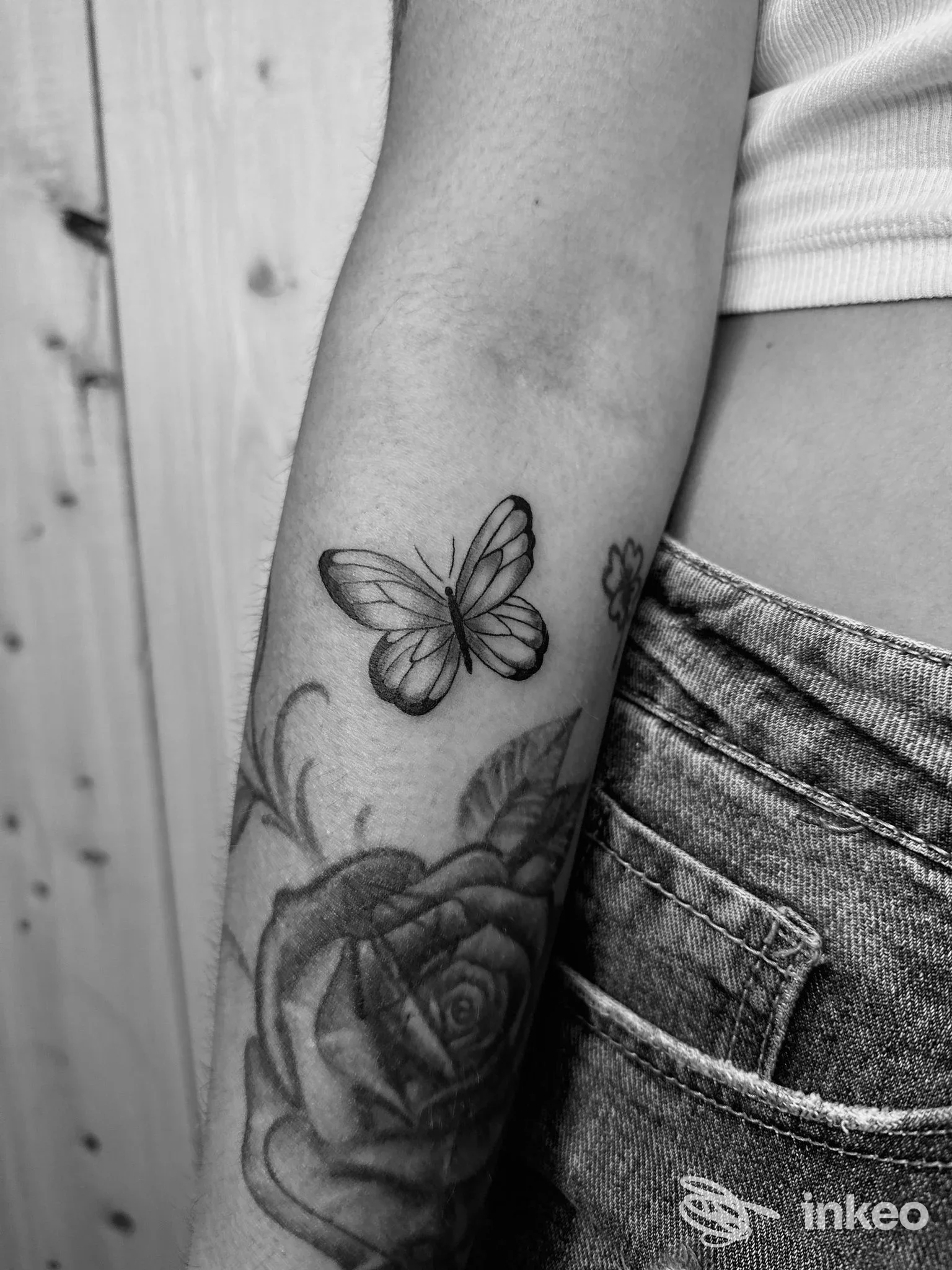 Tatuaggio visibile sull'avambraccio: una rosa accompagnata da una farfalla in bianco e nero, nessun volto visibile.