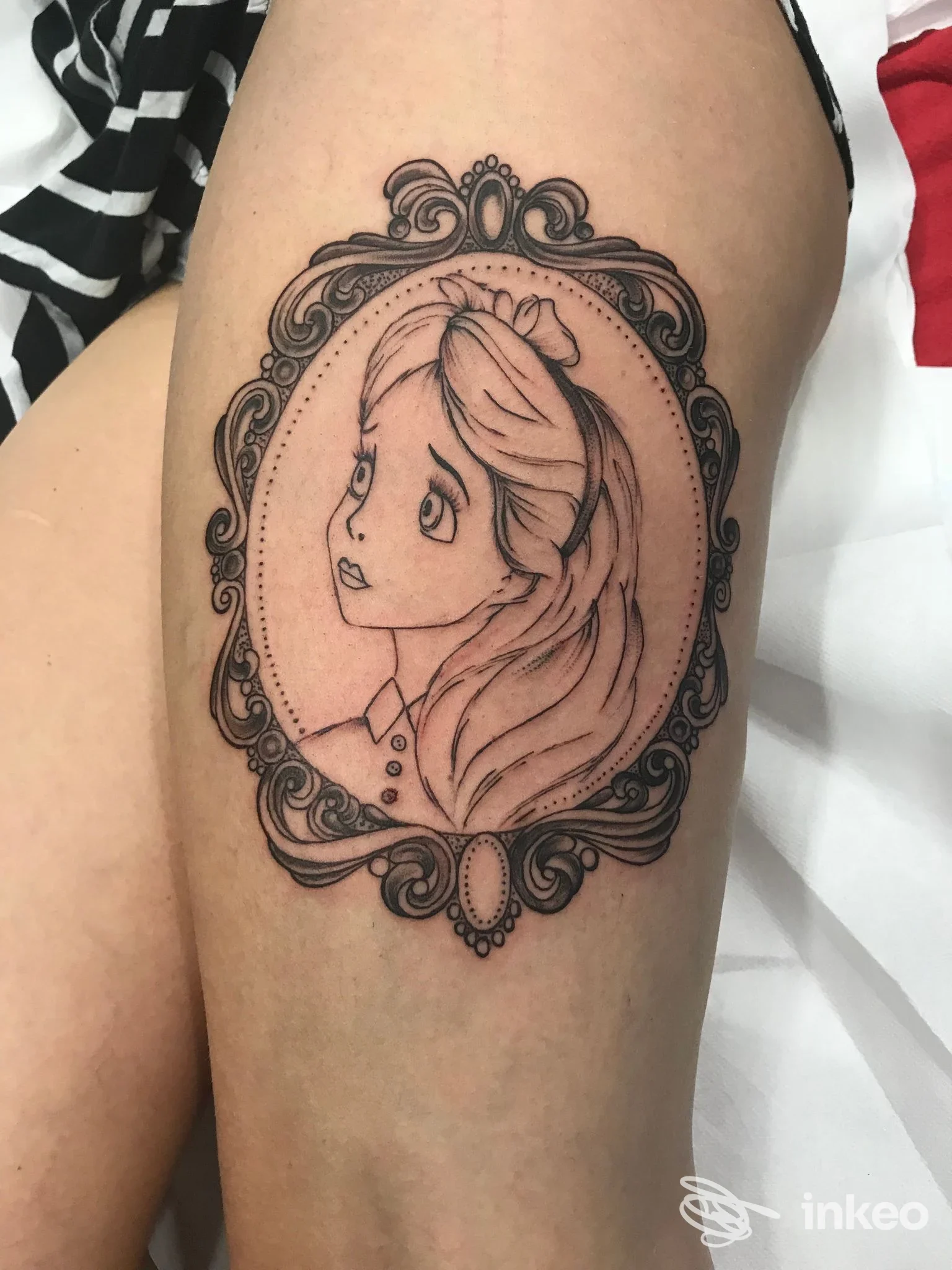 Tatuaggio raffigurante una ragazza in stile disegno, incorniciato in una cornice elaborata, visibile sulla porzione superiore della gamba.