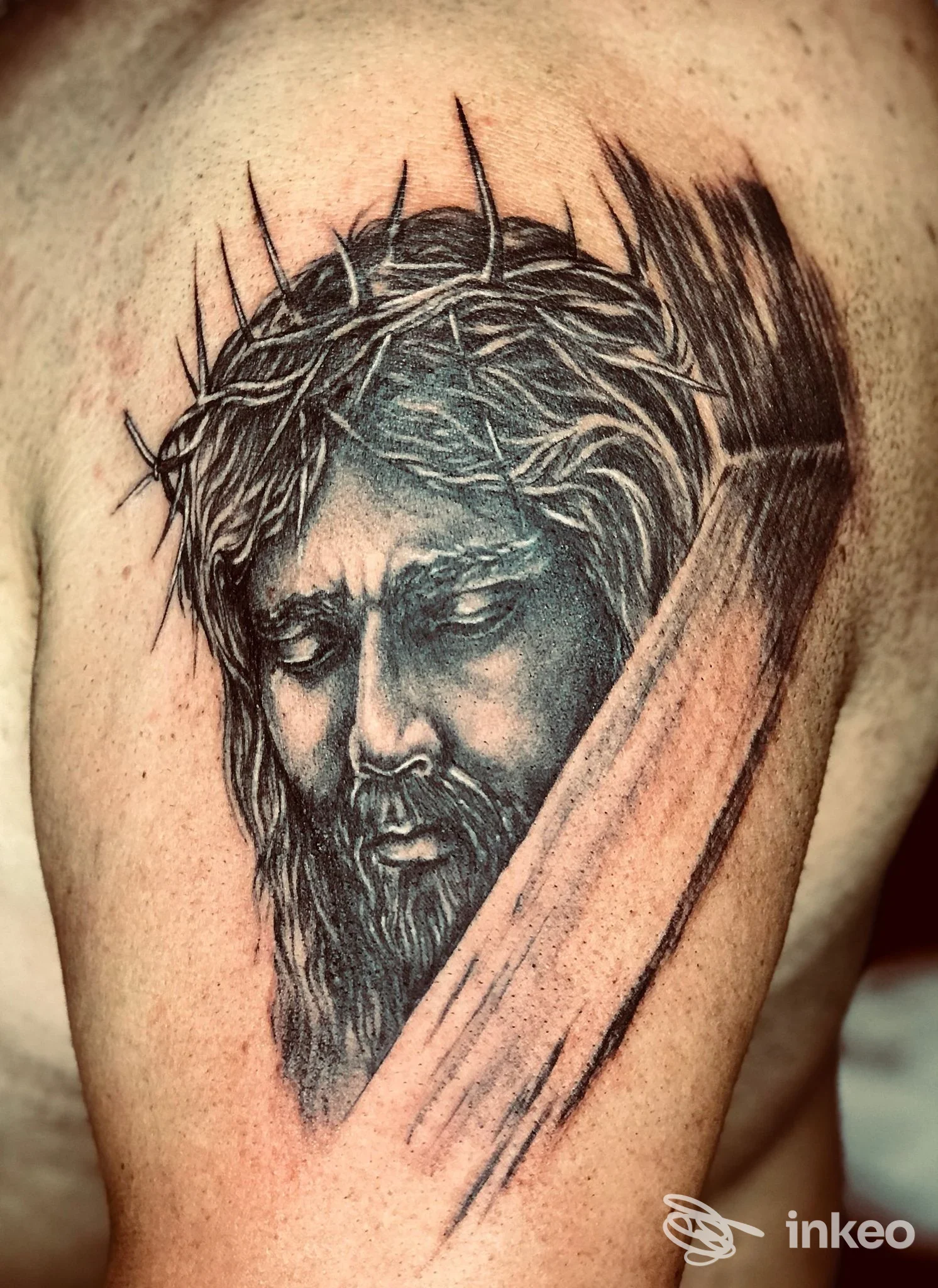 Tattoo realistico su pelle raffigurante Gesù con crocifisso e lama di spada, realizzato sulla spalla/braccio dallstudio Ewa Tattoo di Battipaglia.