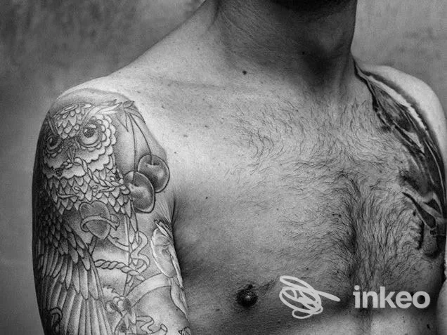 Braccio sinistro di un uomo con tatuaggio ornato visibile sulla spalla e sul torace; testo fonte mostra lo studio Got Art Tattoo Studio a Marano di Napoli.