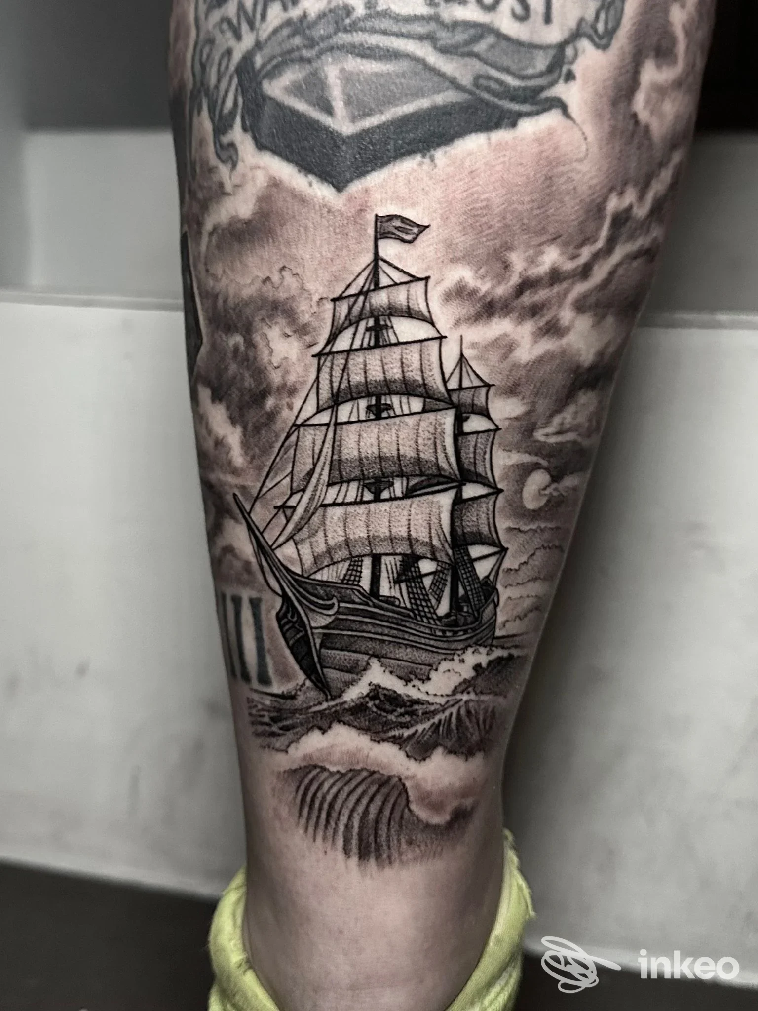 Tatuaggio su pelle della gamba raffigurante una nave a vela in stile nero e grigio, con onde e nuvole sullo sfondo, realizzato a Napoli dall’Asso Tattoo.