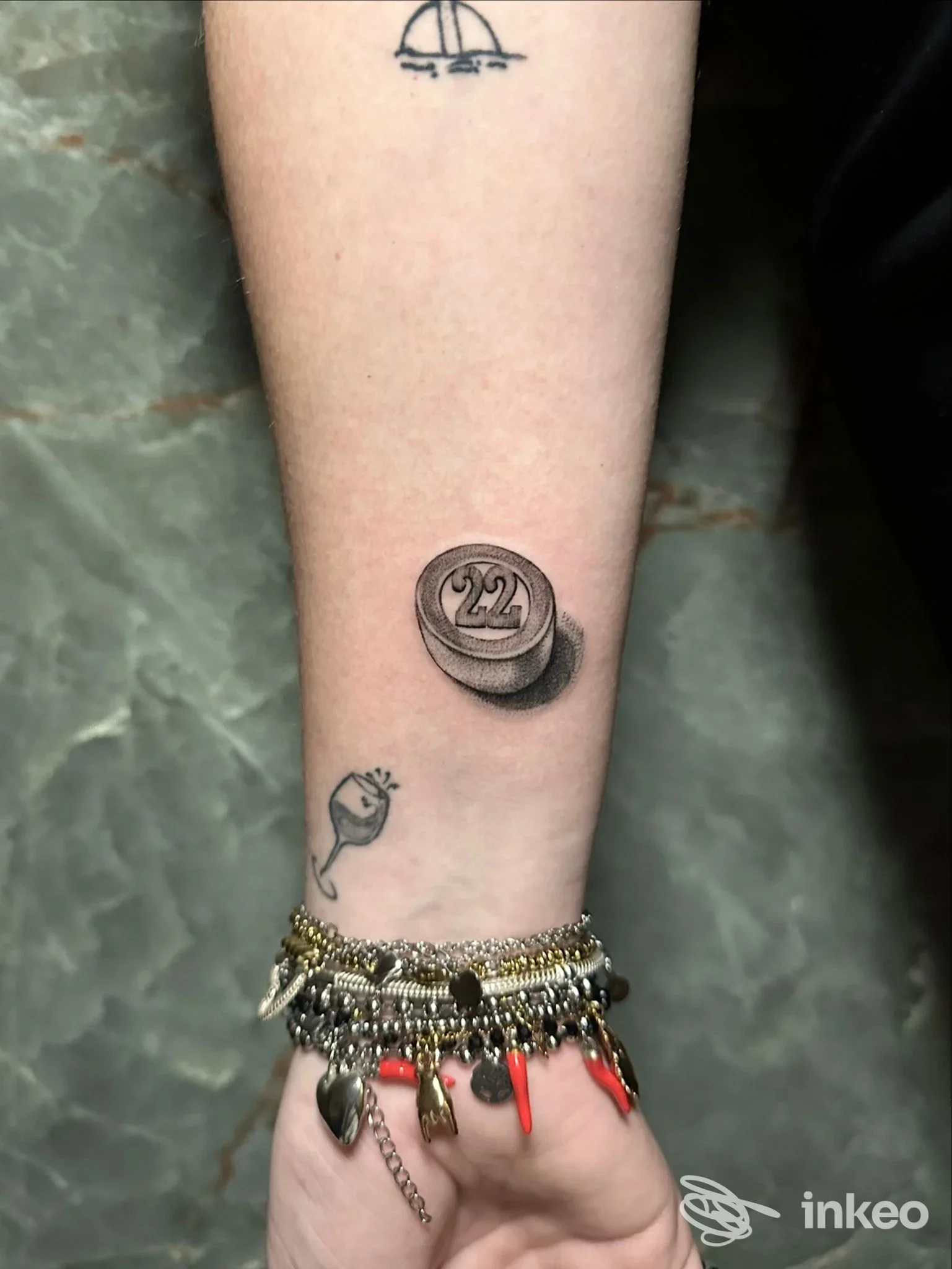 Avambraccio con tatuaggio in bianco e nero di una sfera bombata con marchio 22, oltre a una piccola figura di polpo o chiocciola. Bracciale di braccialetti colorati sul polso. Studio Asso Tattoo Napoli, Napoli.