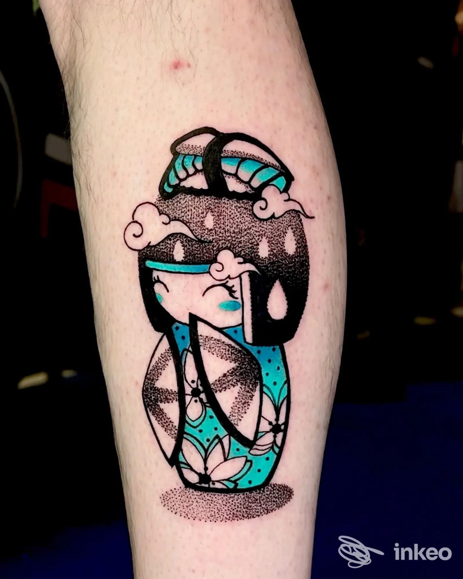Braccio ritratto mostra un tatuaggio colorato in stile geometrico su una forma di vaso o ovala, con linee nere e riempimenti azzurri, senza testo visibile né elementi di social media.
