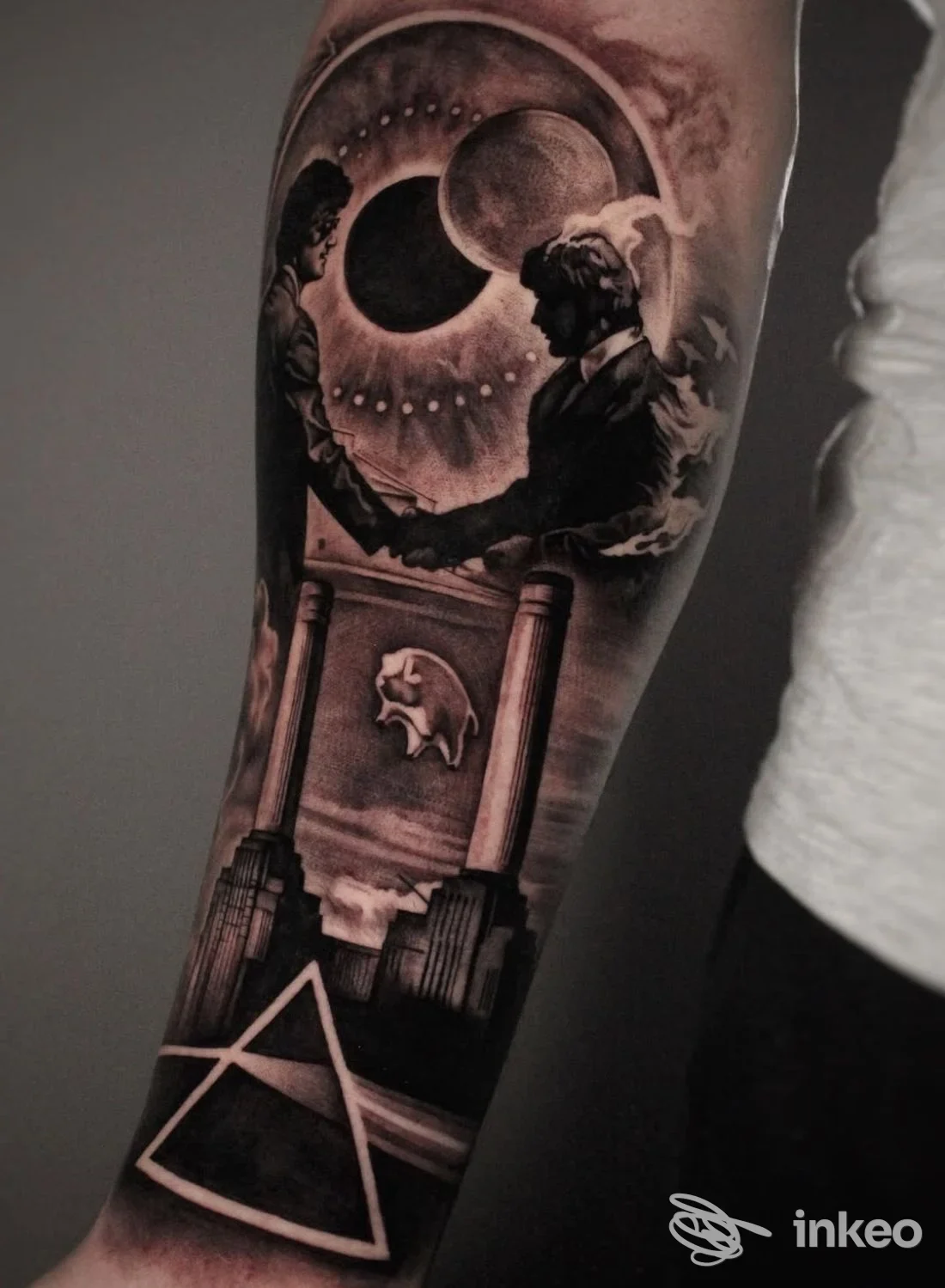 Tatuaggio realistico in bianco e nero sull'avambraccio: figure, colonne architettoniche e simbolo triangolare, sfondo scuro.