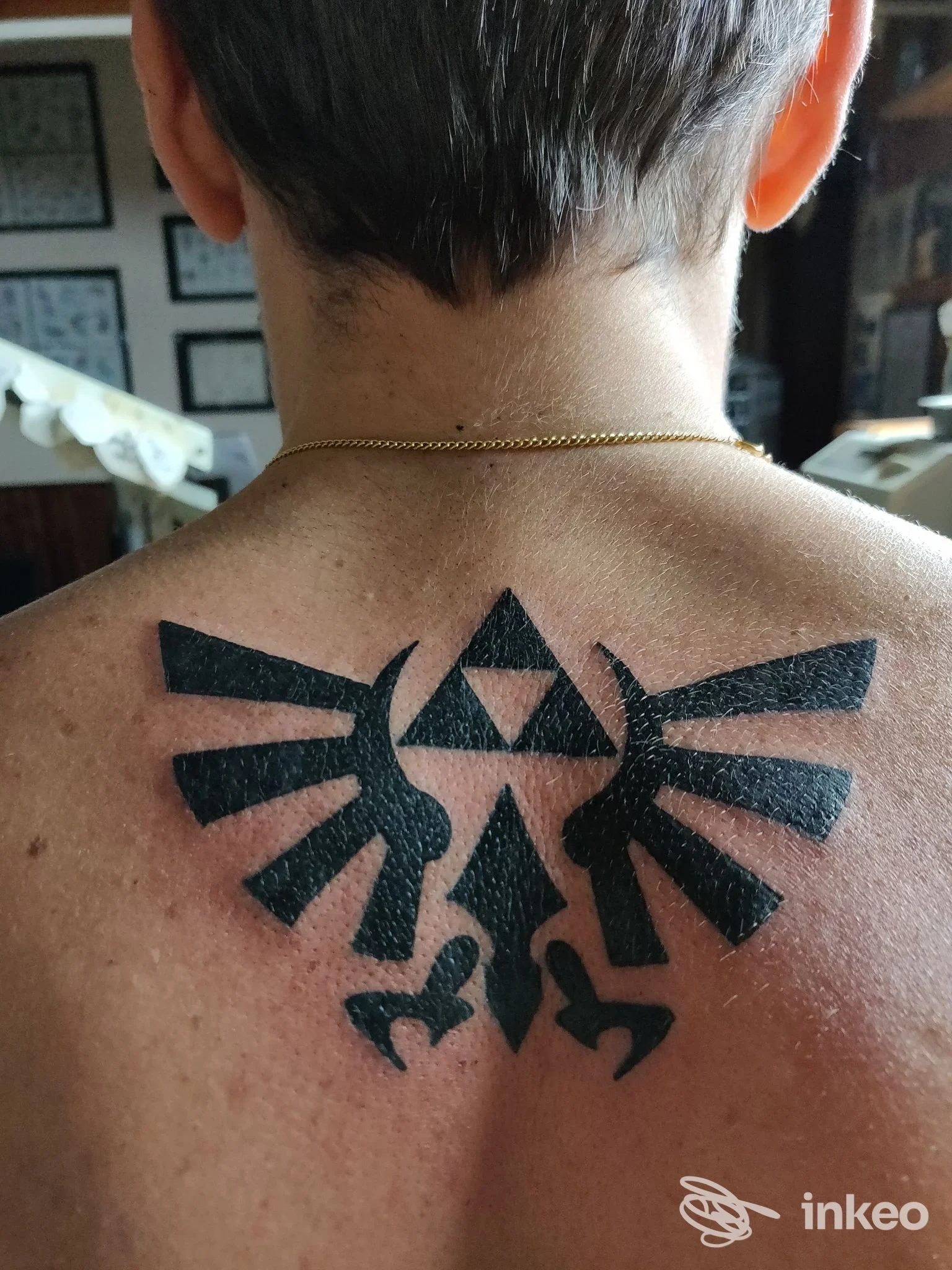 Tattoo visibile sulla nuca di una persona, stilizzazione a aquila nera con scudo centrale; fotogramma a livello di collo, senza volto visibile.