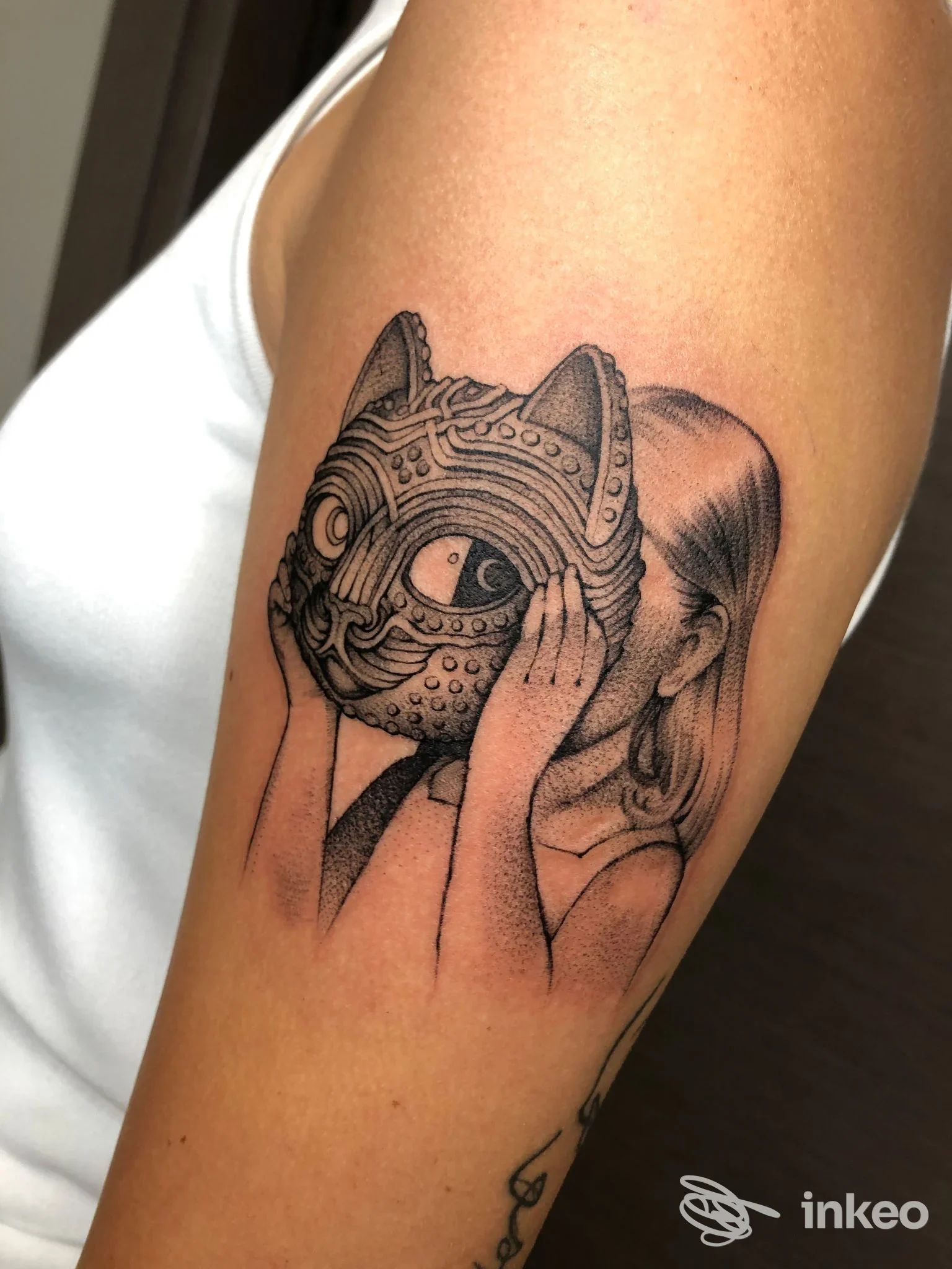 Tattoo sul braccio raffigurante una maschera di gatto in stile disegno puntinato, con mani della persona accanto all'oggetto tatuato, foto singola.