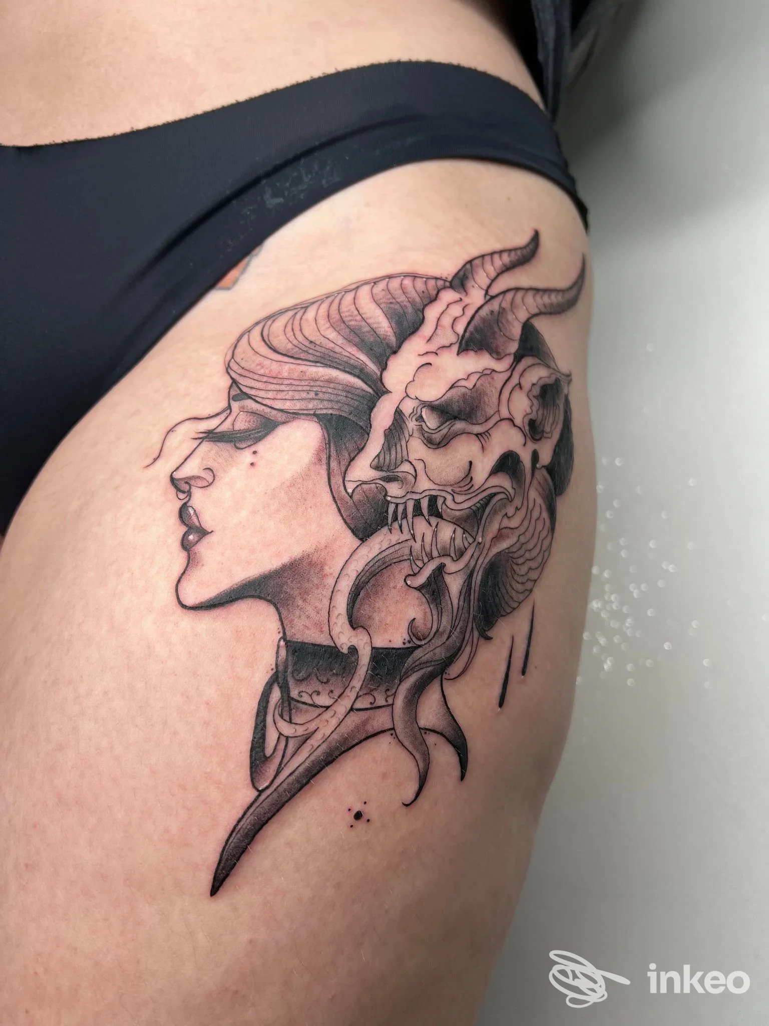 Tattoo in stile ritrattistico su coscia, profilo di una donna con elemento demoniaco; unico pannello, pelle nuda visibile.