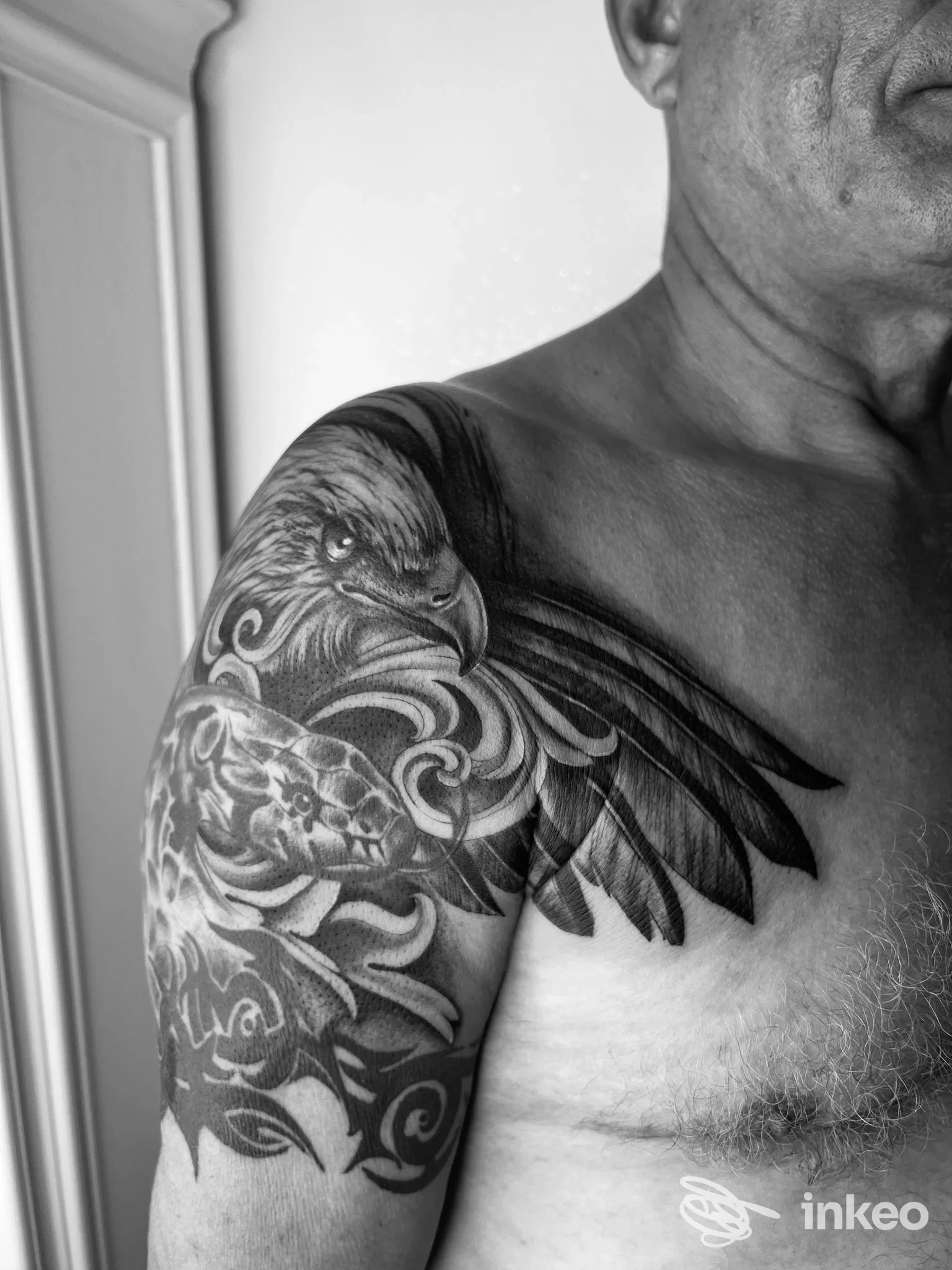 Tatuaggio realistico in bianco e nero sulla spalla e braccio sinistro, disegno ornato con figure di uccello e motivi floreali su pelle umana, in studio.
