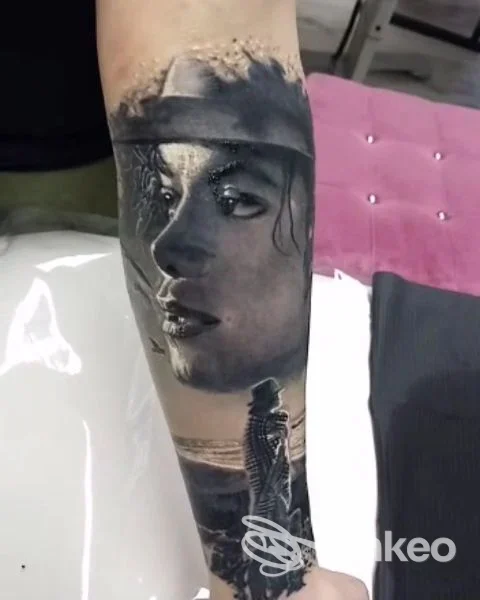 Tattoo realistico sull'avambraccio: ritratto di una donna in primo piano, con scena marina e figura silhouette sullo sfondo.