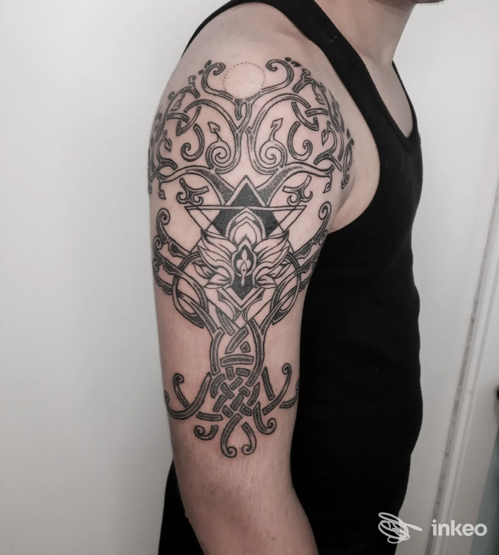 Tattoo integrale sul braccio superiore sinistro, disegno ornato in stile linework con motivi intrecciati e figura centrale geometrica, visibile in primo piano.