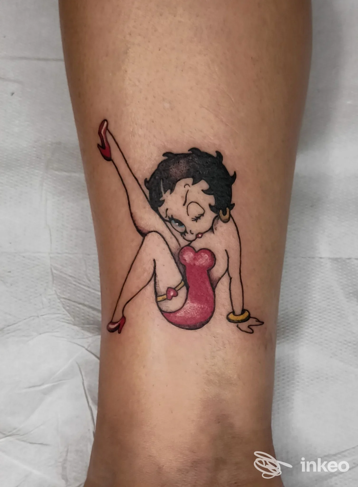 Tattoo su pelle visibile sull’avambraccio/calcio raffigurante una figura femminile con capelli scuri, vestito rosa e braccia sollevate.
