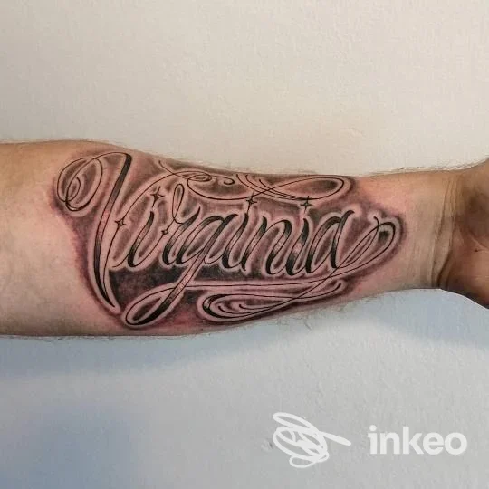 Tatuaggio su avambraccio con la scritta Virginia in stile corsivo, realizzato sulla pelle contro uno sfondo chiaro, senza elementi promozionali.