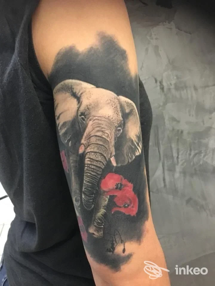 Tatuaggio realistico su braccio di un elefante con sfondo scuro, colori grigi e neri con accenti rosa, senza volto umano visibile.