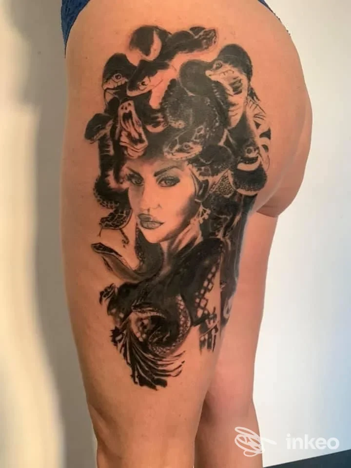 Tattoo su coscia destra raffigurante una figura femminile e serpente, in bianco e nero, con dettagli e sfumature visibili sulla pelle umana.