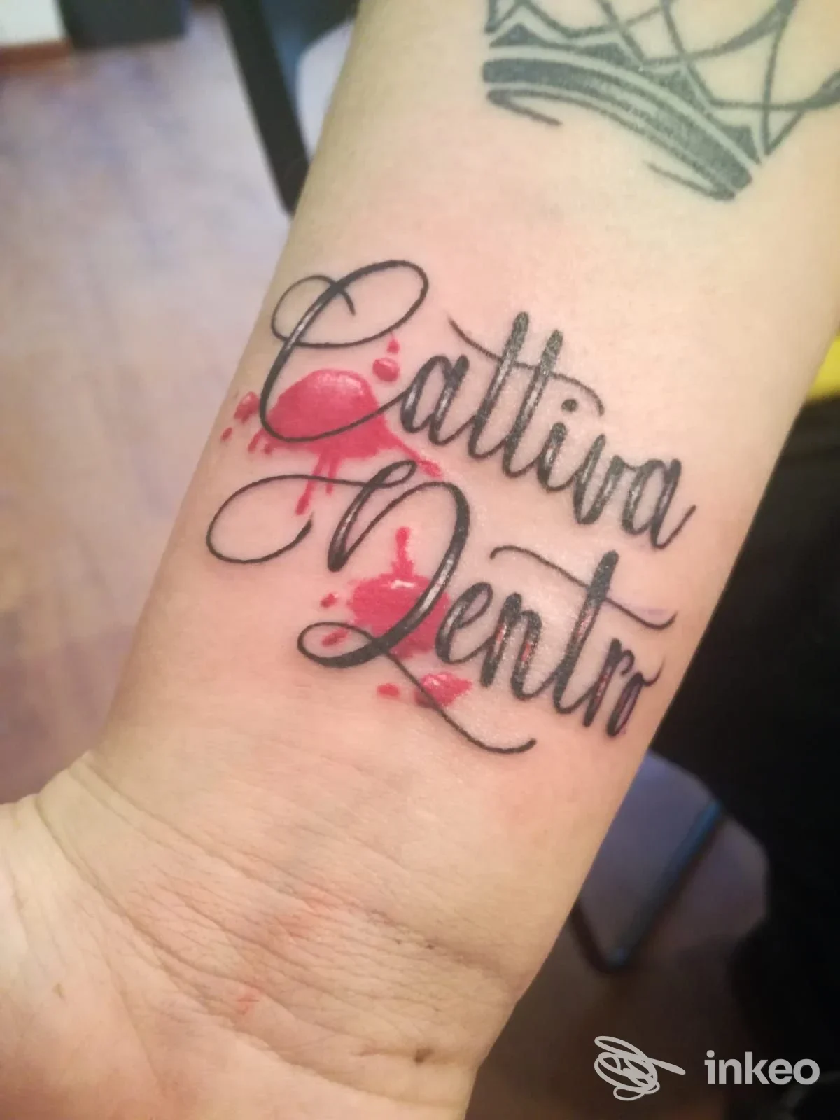Tattoo script su avambraccio con leggere decorazioni rosse, visibile solo l’area del braccio. studio Nosferatu Tatuaggi & Piercing, Reggio nell'Emilia.