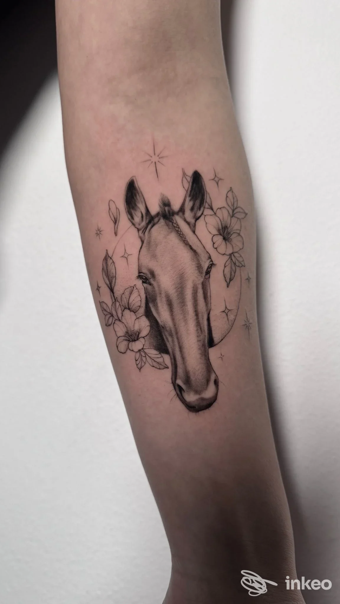 Tatuaggio sul braccio raffigurante una testa di cavallo con fiori intorno, eseguito sulla pelle umana.