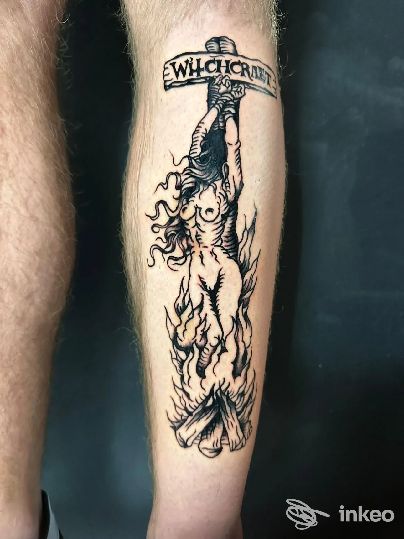 Tatuaggio su pelle visibile lungo una gamba: figura femminile nuda che tiene una bandiera con testo, stile disegno a linee.