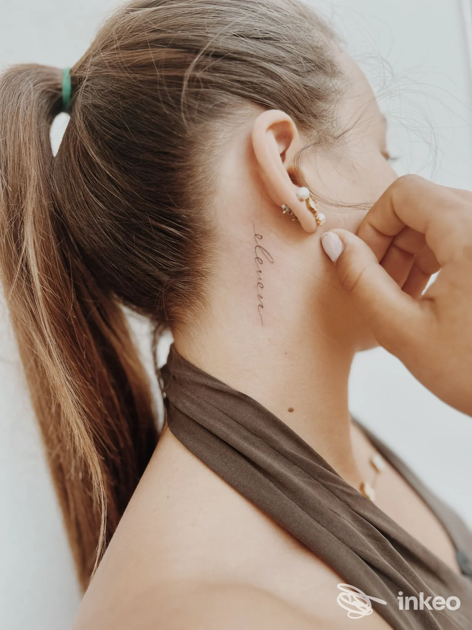Tattoo sul collo visibile lateralmente: una scritta corsiva lungo la nuca, su pelle reale, visibile al lato della testa di una persona in profilo.