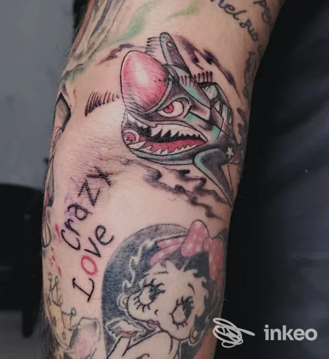 Tatuaggio colorato su braccio raffigurante un drago e Betty Boop, linee definite e colori vivaci visibili sulla pelle.
