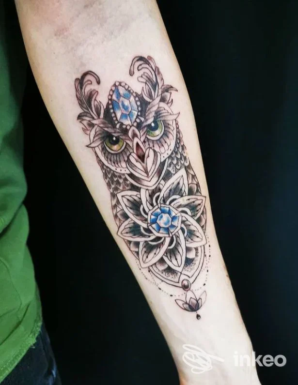 Tatuaggio realistico di gufo con motivi floreali sul polso sinistro, realizzato sulla pelle, colori vividi e linee pulite.